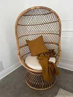 Front view of natural rattan balloon chair with white cushion, mustard throw and pillow draped (throw and pillow not included).