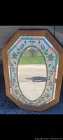 Front view of the octagonal wooden framed mirror showing the oval clear glass mirror surrounded by frosted glass with painted floral and vine design.