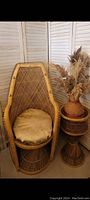 Vintage handmade natural wicker/rattan peacock chair with high curved back and intricate woven pattern. Chair shown with round beige cushion and decorative dried grasses and vase on a matching wicker side table.