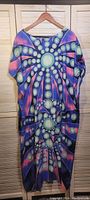 Dress hanging on wooden hanger showing full front with colorful psychedelic geometric pattern and loose fit
