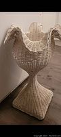 Side view of the white wicker planter showing its tall pedestal base and fluted edges at the top.