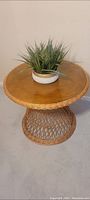 Full view of round wicker table with smooth brown wooden top and decorative plant on top.