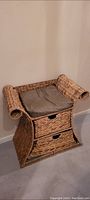 Wicker chair with two drawers and a cushion on the seat, shown from the front and slightly to the side. Curved armrest design visible.