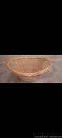 Side view showcasing oval shape and woven wicker construction with handle on left side.