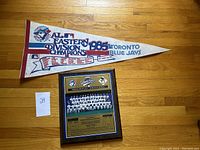 Photo showing the full pennant and the framed team photo plaque on a wooden floor.