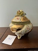 Side view of the Italian lidded bowl showing hand painted floral designs, curved legs, and details on the body.