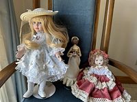 Photo showing three collectible dolls on a chair, displaying their size, dress details and conditions.