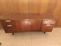 Photo of wooden desk against a wood paneled wall, showing front view with drawers and sliding door cabinet closed.