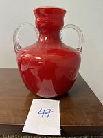 Front view of the red glass vase showing the rounded body and neck with two clear loop handles.