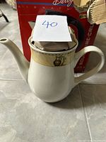 Close-up of ceramic coffee pot with decorative beige and gold band featuring a coffee pot motif, lid visible on top