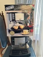 Photo of DeLonghi Caffè Venezia espresso machine with original packaging box on top, showing product image and branding.
