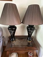 Pair of black ceramic lamps with brown pleated shades on a wooden table.