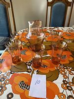 Set of one pink glass pitcher with handle and six matching pink glasses shown on a floral tablecloth.