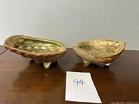 Pair of natural shell art bowls resting on a wooden surface, showing the size relative to a small numbered paper.