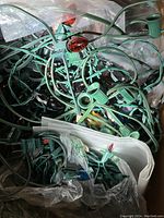 Tangled strands of green wired Christmas lights with red, black, and clear bulbs visible, some plastic bags in background.
