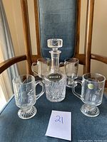 Full set photo showing one crystal decanter with stopper and four matching crystal glasses arranged on a wooden chair with blue cushion.