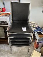 Stack of five black chairs with chrome frames showing front and top view of seat and backrest surfaces.