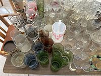 Top view of a large assortment of clear, tinted, and printed drinking glasses, cups, and some plastic containers on a table.