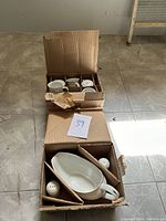Boxed white ceramic dish set items on tiled floor showing gravy boat and salt and pepper shakers.