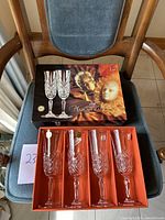 Four crystal champagne flute glasses displayed in original Masquerade box on chair, showing ornate cut crystal design and decorative packaging.