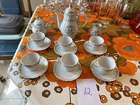 Full tea set including teapot, sugar bowl, creamer, 5 cups, and 5 saucers on table with floral tablecloth.