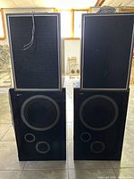 Front view of two pairs of speakers stacked, showing black fabric grills framed in silver with minor wear.