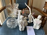 Overview photo showing various white ceramic and clear glass home decor pieces arranged on a chair.