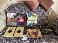 Photo of all ten books arranged on a couch showing covers including The Guinness Encyclopedia, The Incredible Machine, Atlas of Canada and the Modern World encyclopedia volumes, plus four large nature books with photographic covers.