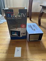 Vintage Ken-Tech 5" color TV with AM/FM radio next to its original packaging box on wooden floor.