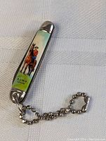 Photo showing closed pocket knife with RCMP officer on horseback graphic and attached ball chain keychain.