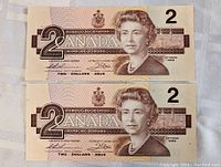 Two sequential 1986 Canadian two dollar bills, front side showing Queen Elizabeth II, serial numbers visible, uncirculated condition.