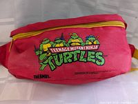 Front view of red fanny pack featuring colorful Teenage Mutant Ninja Turtles graphic with yellow zipper and strap.