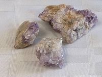 Three amethyst crystal mineral specimens on light fabric background showing size and color details