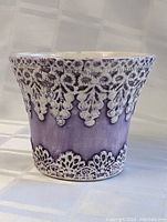 Front view of purple glazed pottery planter with raised white floral decorative patterns around the rim and base.
