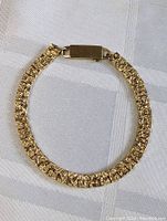 Full view of the chunky vintage gold plated bracelet by MCM lying flat on a white textured surface.