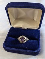Vintage sterling silver ring with purple amethyst set in detailed filigree frame inside a blue velvet box.