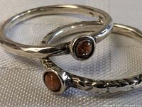 Close-up of two hammered sterling silver rings with small brown stones inset, showing texture and carved details