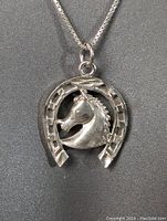 Close-up of sterling silver pendant showing detailed carving of horse stallion head in horseshoe