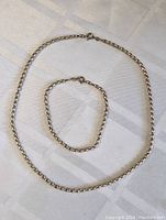 Full view of sterling silver necklace and bracelet laid flat showing the overall shape and chain links.