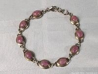 Close-up of sterling silver pink jadeite bracelet showing the linked oval stone settings and clasp on a light fabric background.