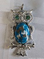 Front view of vintage owl pendant showing green jeweled eyes, blue stone body with matrix, and silver-tone metal detailing.