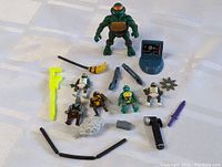 TMNT figures and accessories laid out on a white surface showing the variety of miniatures and weapons included in the lot.
