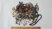 Overview image showing a large assortment of costume jewelry including chains, pendants, and earrings spread out on a white background with a ruler for scale.
