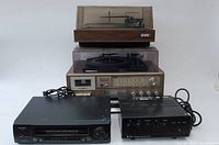 Front and top view of black Sharp VHS player, black TOA amplifier, silver Realistic stereo receiver with wood-veneer Realistic turntable on top, and a beige Yorx stereo turntable below the Realistic turntable.