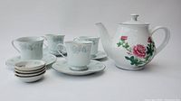 Overall view showing white ceramic teapot and set of four cups with saucers and small plates