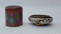 Photo of red cylindrical cloisonne jar with lid and white floral cloisonne bowl side by side