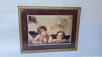 Full view of the framed print showing the two cherubs from the Sistine Chapel. The frame has a decorative gold finish and maroon mat.