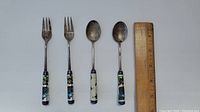 Top view of the 2 forks and 2 spoons with cloisonné handles and a ruler for scale showing approximately 4.5 inches length.