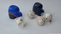 Photo showing multiple mini MLB helmets grouped into two stacks, and four replica signed baseballs, two of which are in plastic wrap.