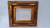 Front view of ornate wooden picture frame showing carved details and gold finish.